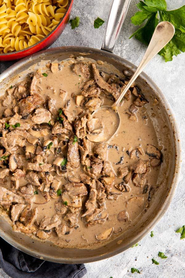 Pfanne mit Rindsgeschnetzeltem Stroganoff, daneben ein Topf mit Nudeln