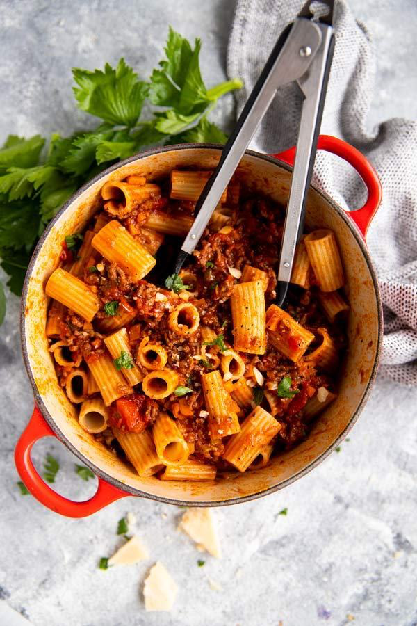 roter gusseiserner Topf, gefüllt mit Rigatoni in Bolognese Sauce