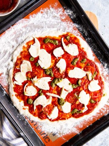 ungebackene Pizza auf einem Blech mit Silikon-Backmatte