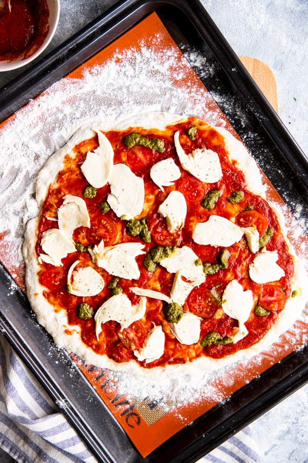 ungebackene Pizza auf einem Blech mit Silikon-Backmatte