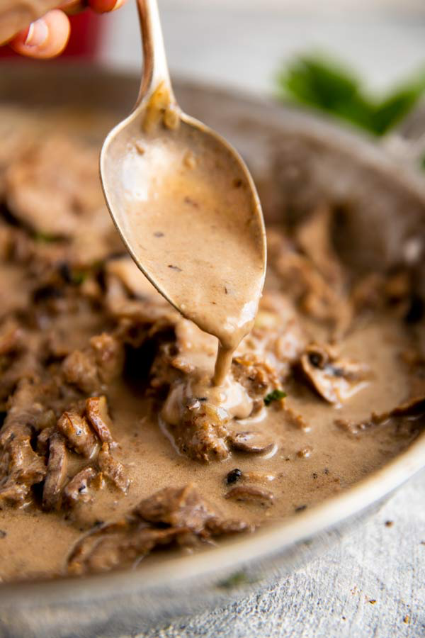 Stroganoff-Sauce läuft von einem Löffel auf das Fleisch