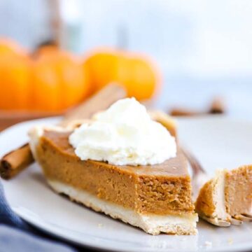 Pumpkin Pie auf einem Teller mit ener Gabel und Kürbissen im Hintergrund