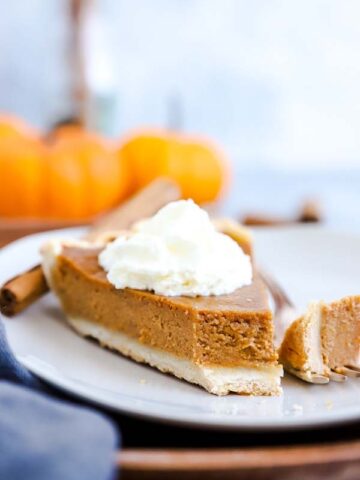 Pumpkin Pie auf einem Teller mit ener Gabel und Kürbissen im Hintergrund