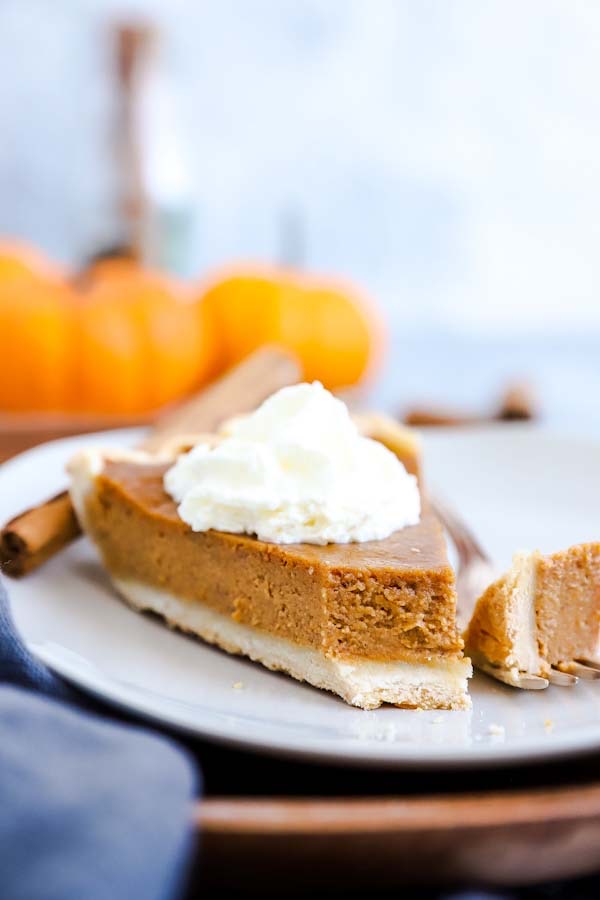 Pumpkin Pie auf einem Teller mit ener Gabel und Kürbissen im Hintergrund