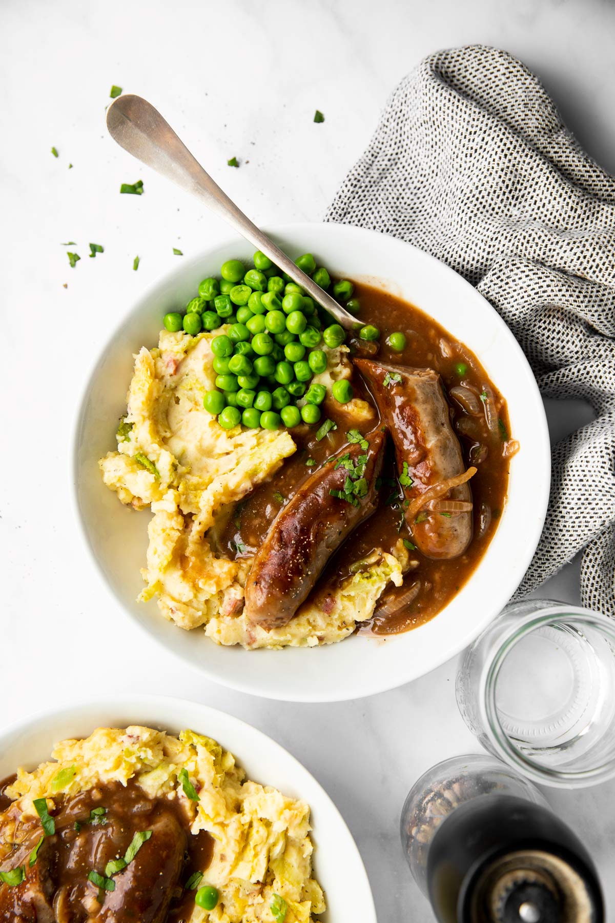 Teller mit Bratwurst, Zwiebelsauce, Kartoffelbrei und Erbsen auf einem Marmortisch