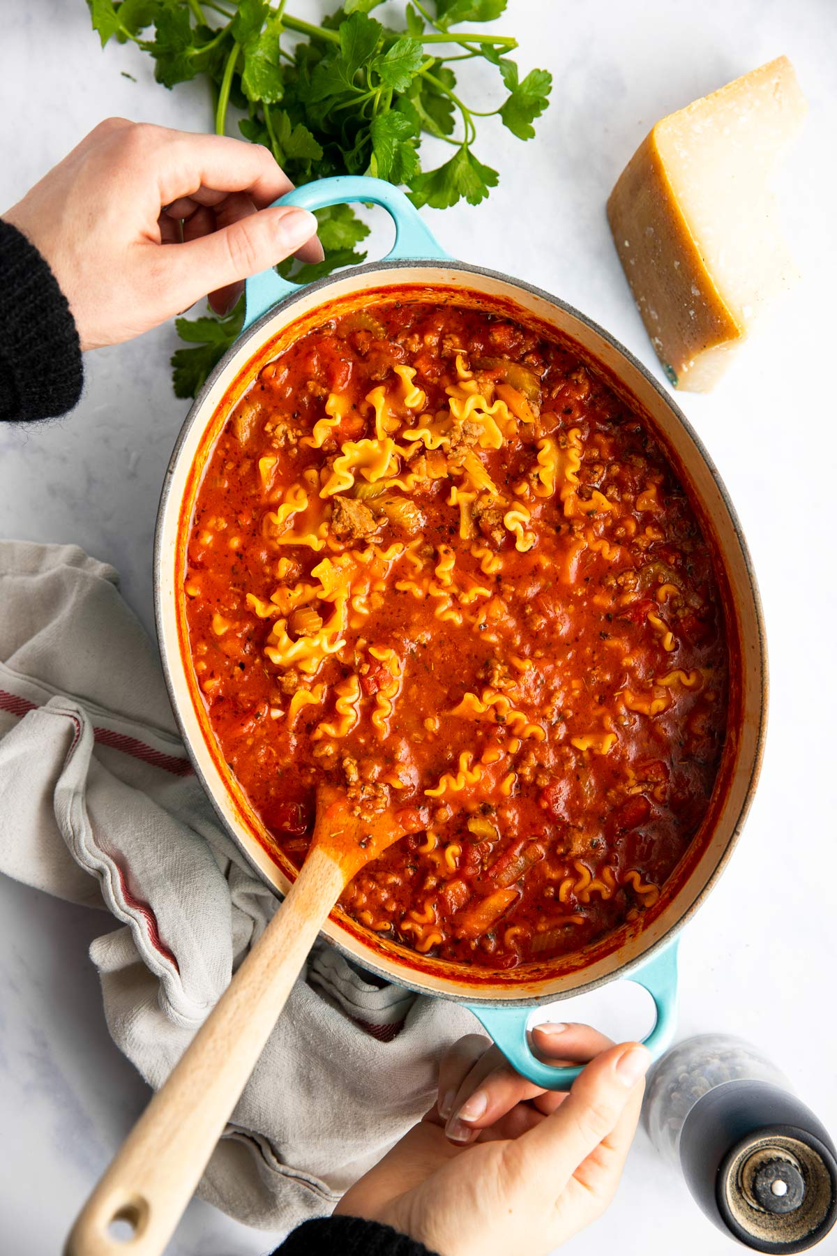 Frau hält Topf mit Lasagnesuppe auf einer Marmorplatte