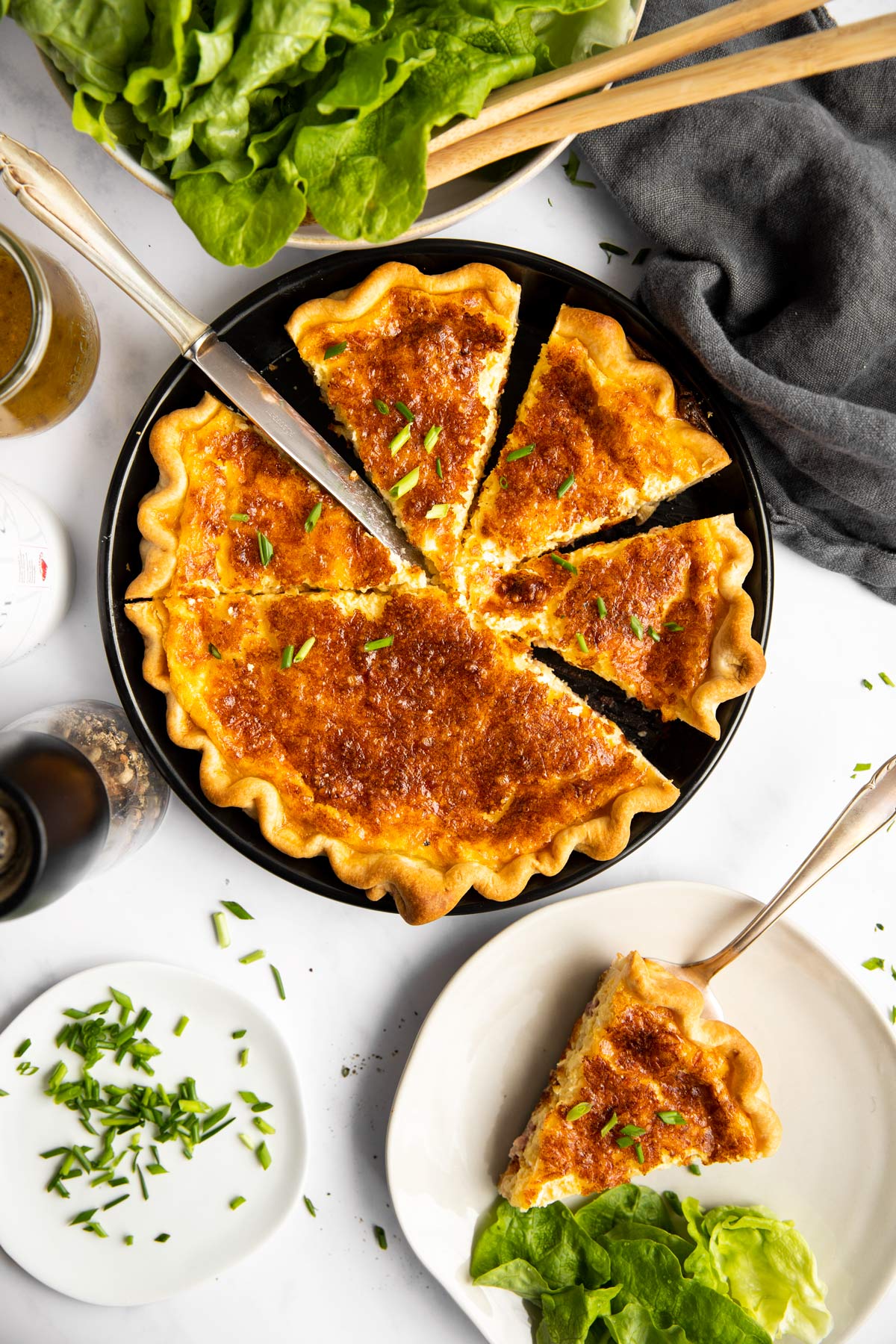 geschnittene Quiche Lorraine von oben auf einem Tisch mit Salat und Tellern