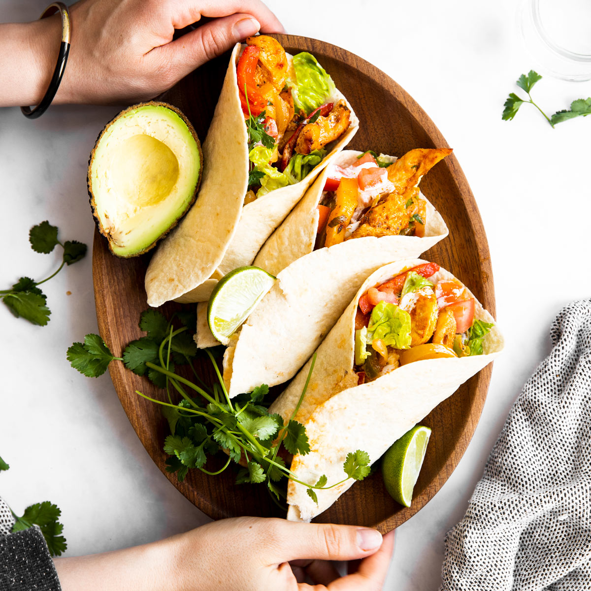 Sicht von Oben auf Frauenhände, die eine Platte mit Fajitas halten