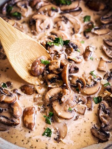 Nahaufnahme von Rahmchampignons in Pfanne mit Holzlöffel