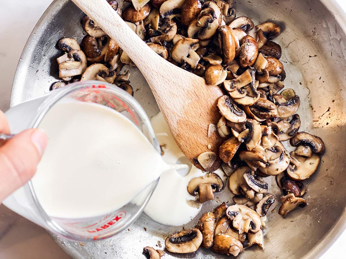 Sahne wird aus gläsernem Messbecher zu Champignons in Pfanne gegossen