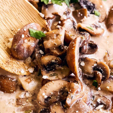 Nahaufnahme von Rahmchampignons in Pfanne mit Holzlöffel